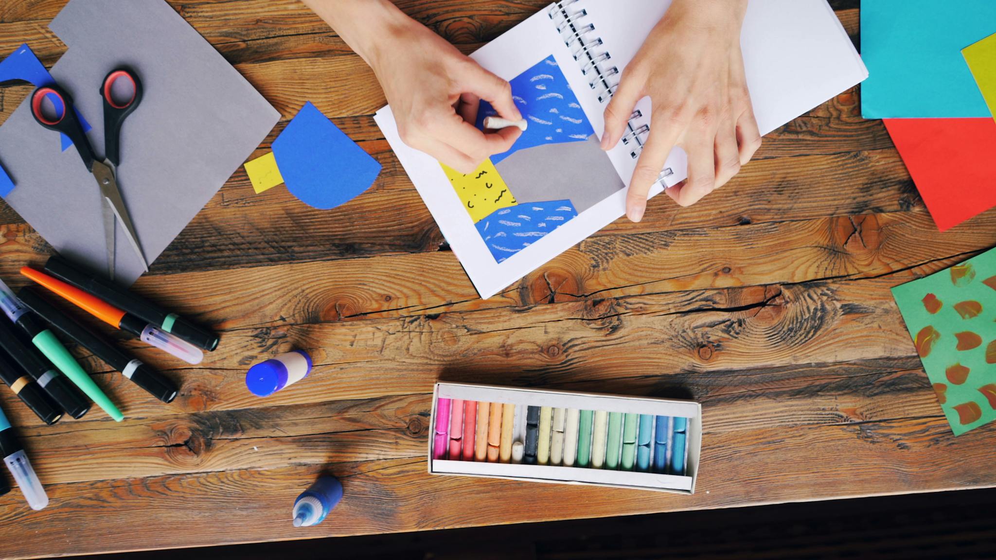 A vibrant arts and crafts setup with colorful papers and pastel colors on a wooden table.