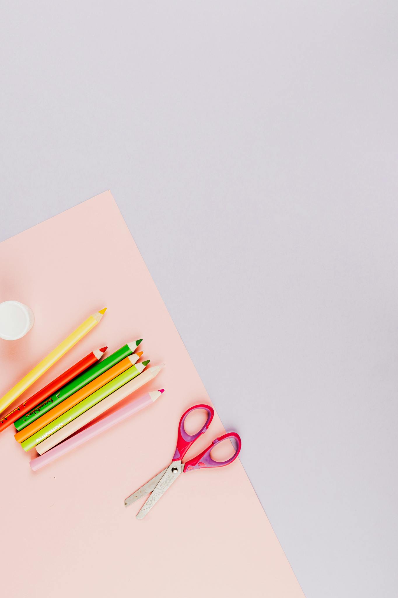 Bright art supplies including colored pencils and scissors on peach paper with ample copy space.