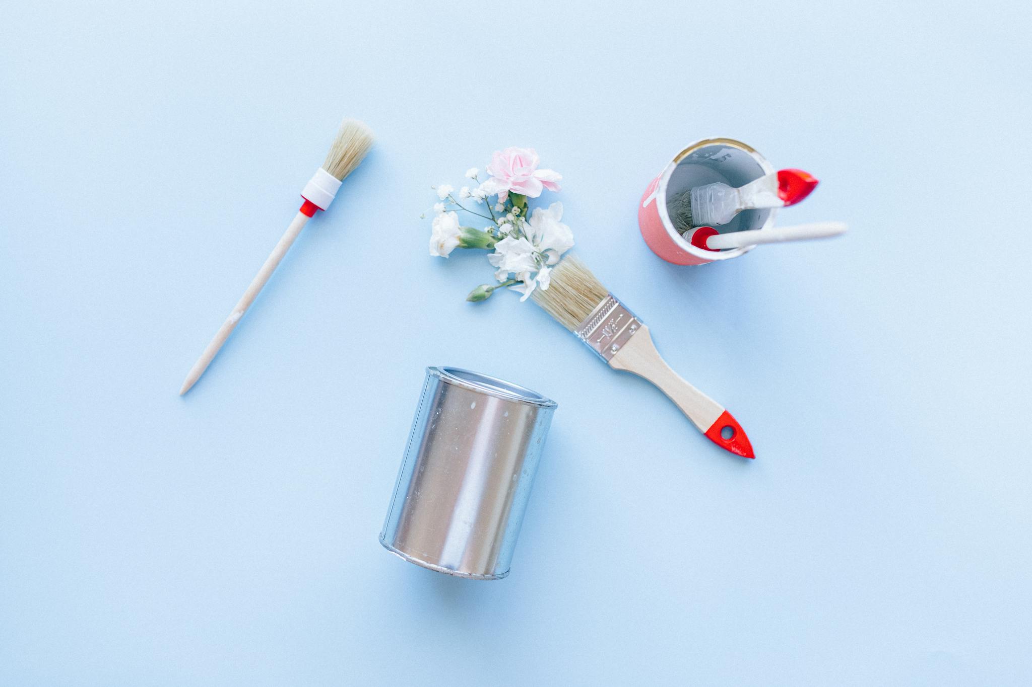 Creative top view of paintbrushes, cans, and flowers against a light blue background.