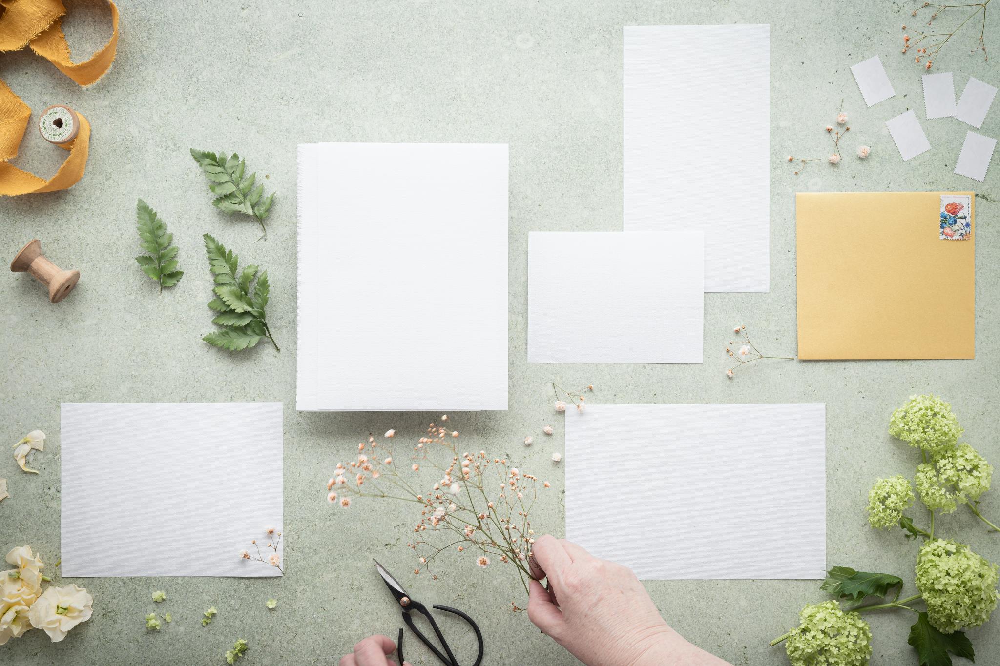 Inspiring flat lay of blank paper, greenery, and flowers ideal for DIY and craft projects.
