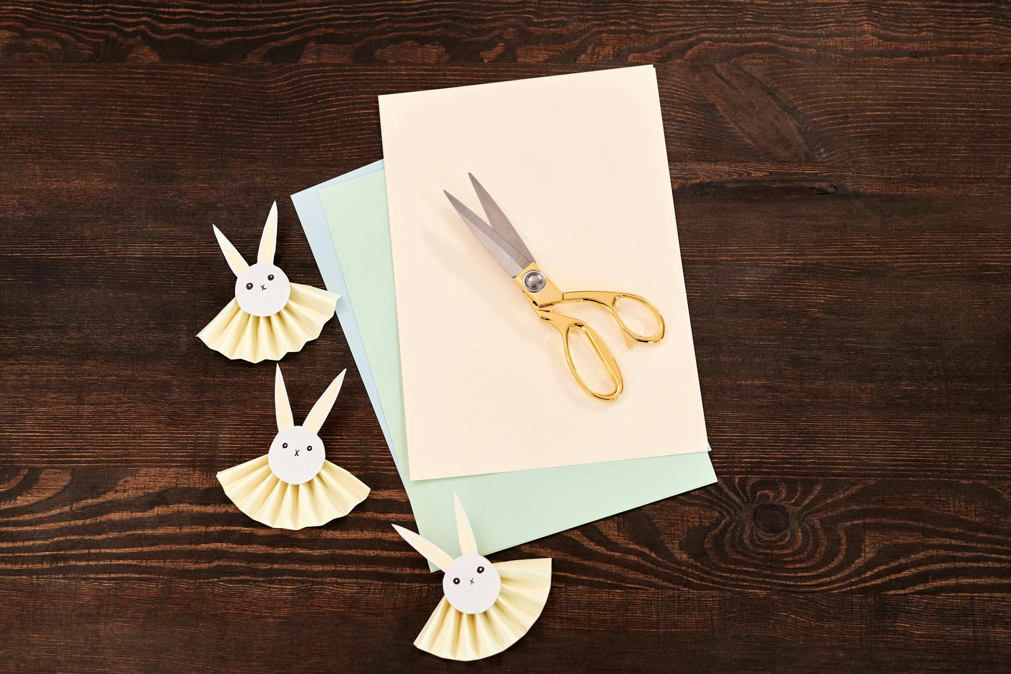 Top view of paper bunny crafts and scissors on wooden surface, perfect for Easter DIY projects.