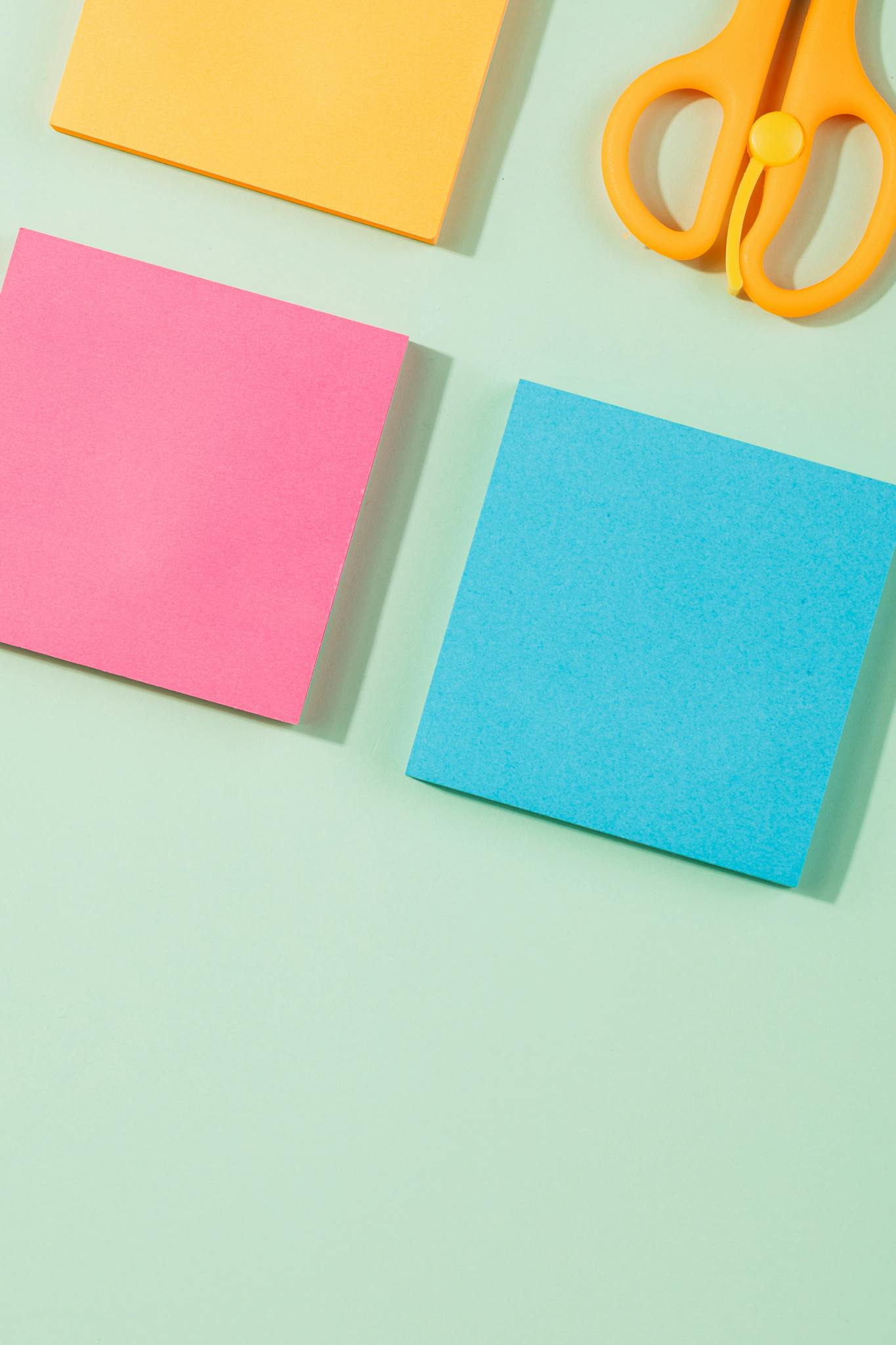 Vibrant sticky notes and scissors arranged on a pastel green background for creative projects.